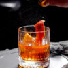 close up crystal viski glass with alcohol cocktail garnished with orange zest